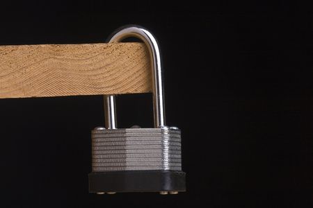 Metal lock attached to a piece of wood on a black background.の写真素材