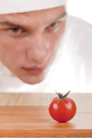 The young chef in chef's hat is considering a tomato.の写真素材