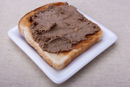 Liver pate on a piece of toasted white bread on a white plate.の写真素材