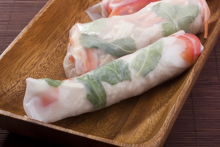 Asian spring rolls in rice paper on a wooden plate.