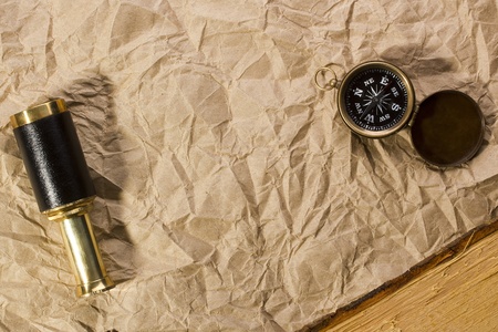 A golden compass and a spyglass laying on an old wrinkled brown paper that can serve as a background...