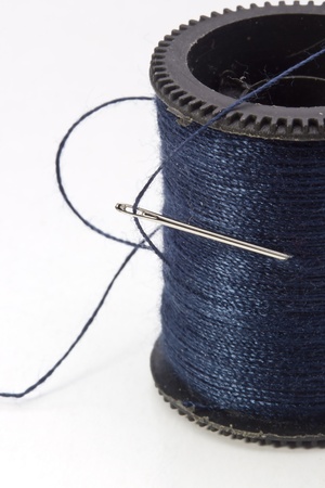 Close-up photograph of a blue thread spool and needle.