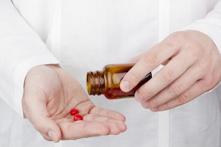 Close-up photograph of a hand pouring red tablets out of a transparent bottle into another hand.の写真素材