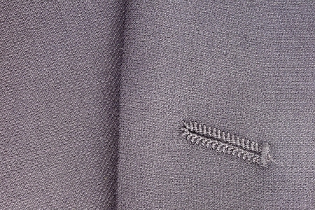 Close-up photograph of a button hole on gray fabric.