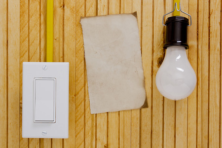 Light bulb, switch wall and wooden background with a sheet of old paper.