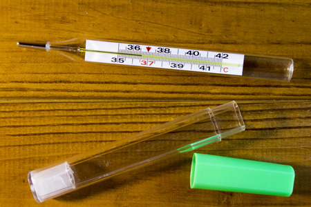 Mercury thermometer to monitor the temperature of the body on a wooden table.