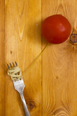 Pasta wrapped around fork and a tomato on a wooden backgroundの写真素材