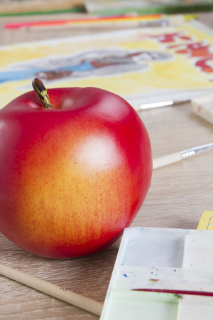Red apple and pencils, paints and drawingsの写真素材