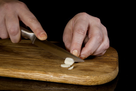 Woman chopping garlic with a knife on a wooden boardの写真素材