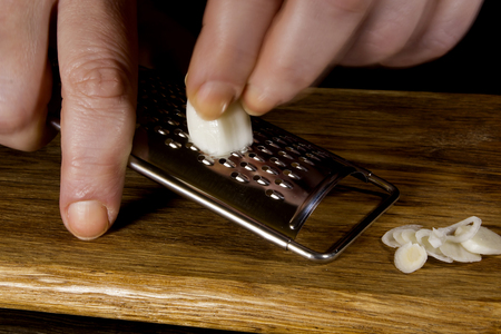 Female hands grind garlic on a grater on a black backgroundの写真素材
