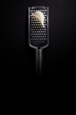 Metallic shiny grater and garlic on a black backgroundの写真素材
