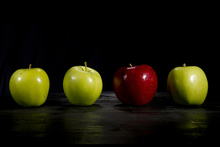 Red apple standing out in a row of green applesの写真素材