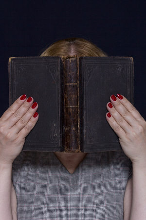 The hands of a young woman hold the book in front of the faceの写真素材