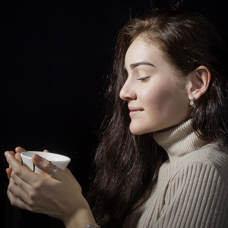 Portrait of a young beautiful woman with a cup of coffee on a black backgroundの写真素材