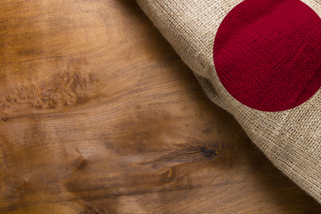 A flag of Japan made from rough fabric on a wooden background.の写真素材