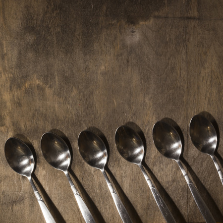 A row of metal spoons on a wooden old backgroundの写真素材