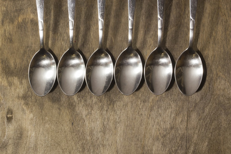 A row of metal spoons on a wooden old backgroundの写真素材