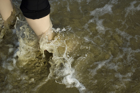 Sea foam waves wash women's feet on the beachの写真素材