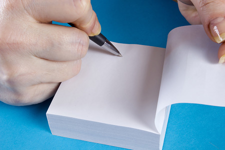 Female hands and a block for taking notes on a blue surface