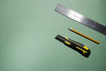 Construction knife, ruler and pencil on a green background