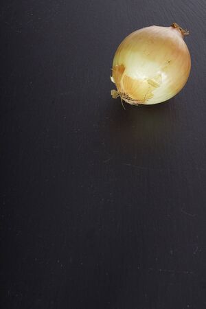 Ripe onion in husk on a black stone cutting boardの写真素材