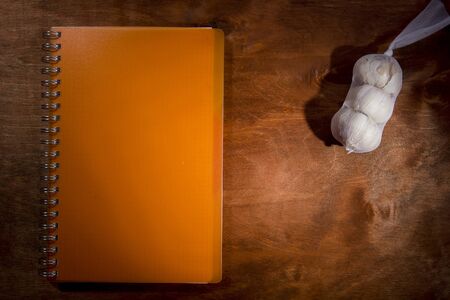Garlic heads and orange notebook on a wooden tableの写真素材