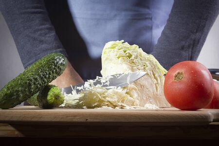 Hands with a knife chopping cabbage on the kitchen tableの写真素材