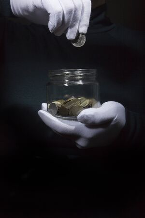 Hand in a white glove throws a coin into a glass jar