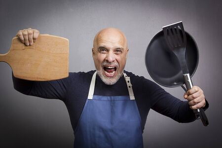Gray-haired man with kitchen equipment on gray backgroundの写真素材