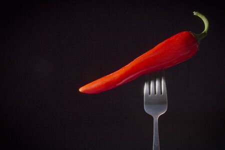 Red chili peppers impaled on a fork on a black backgroundの写真素材