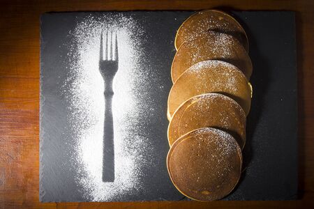 Pancakes and icing sugar on a black stone boardの写真素材