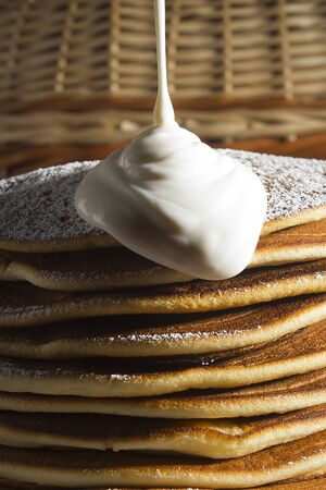 A pile of pancakes with sour cream on a wicker basket background