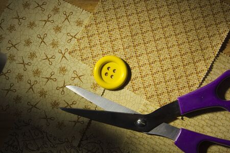 Scissors and a button on the background of fragments of fabricの写真素材