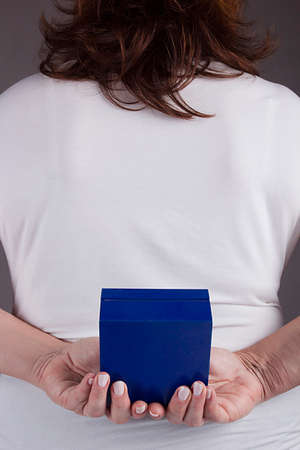 Woman with a gift behind her back on a gray backgroundの写真素材