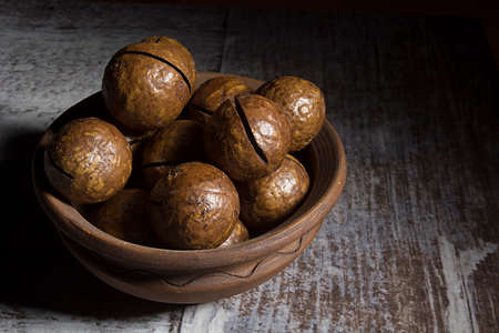Macadamia nuts in shells in earthenware dish on wooden table