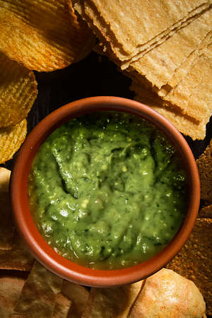 Green guacamole sauce in pottery and assorted chips