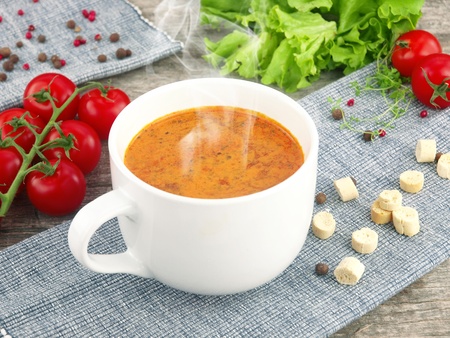 Tomato soup with fresh ingredients in a soup cup, over an old wooden background の写真素材