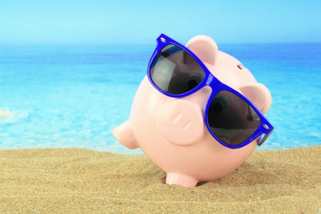 Summer piggy bank with sunglasses on the beach の写真素材