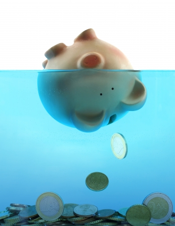 Drowning in debt represented by a piggy bank sinking in blue waterの写真素材