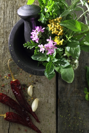 Black stone mortar and pestle with fresh herbs on old wooden backgroundの写真素材