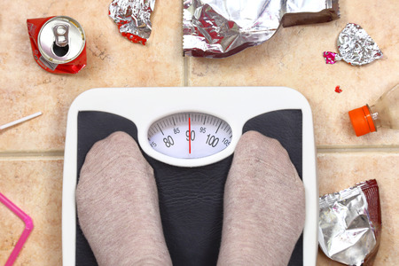 Feet on bathroom scale with junk food garbage aroundの写真素材
