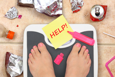 Feet on bathroom scale with word Help and junk food garbageの写真素材