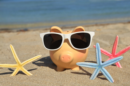 Summer piggy bank with sunglasses on the sandの写真素材