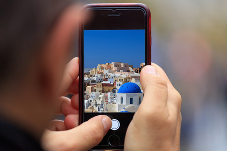 Greece, Santorini's traditional houses picture appear on tablet, smartphone in man's hands. Blurred backgroundの写真素材