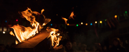 Bonfire with colorful flames and bokeh lights. Big blaze with firewoods. Blurred people on night...
