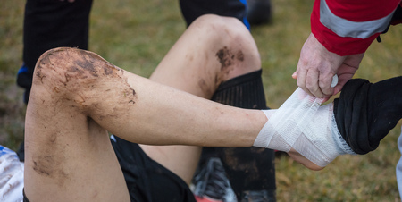 Soccer, football concept. Injured footballer lay down on field. Physiotherapist puts bandage on his ankle. Blurred background, close up view.の写真素材