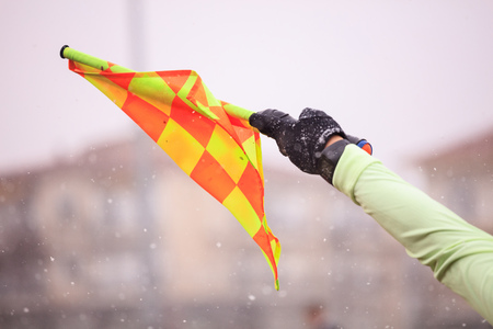 Soccer football referee assistant raises the flag. Blurred snowy background, close up view.