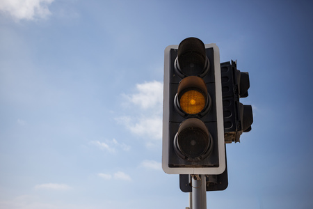 Yellow, orange color traffic light. Blue sky with few clouds background. Close up under view, space...