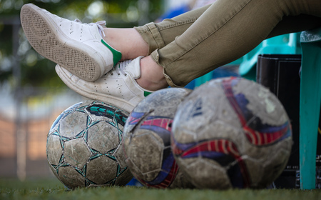 Football concept. Football soccer game onlooker sports fan resting on bench on worn out football balls in the field, blurry background and wallpaper.の写真素材
