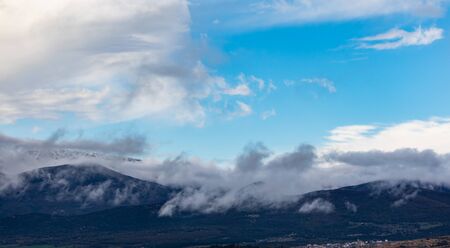 Mountains full of trees and  clouds cover the tops of snowy mountains